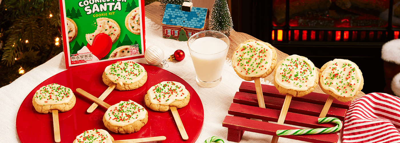 delicious cookie pops for Santa garnished with icing & colorful sprinkles served on a red plate on a Christmas decorated table