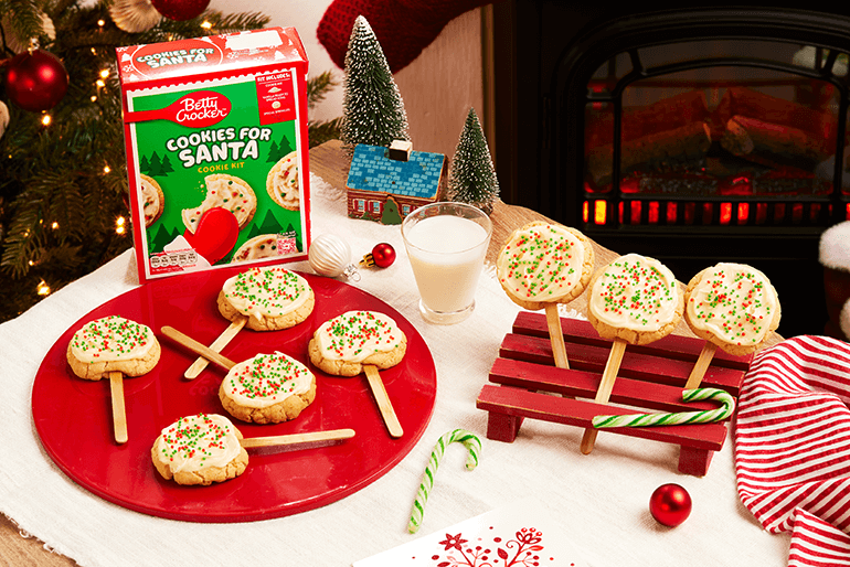 delicious cookie pops for Santa garnished with cream & colorful sprinkles served on a red plate on a Christmas decorated table