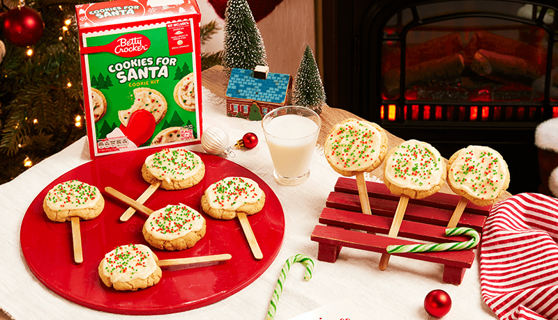 delicious cookie pops for Santa garnished with cream & colorful sprinkles served on a red plate on a Christmas decorated table