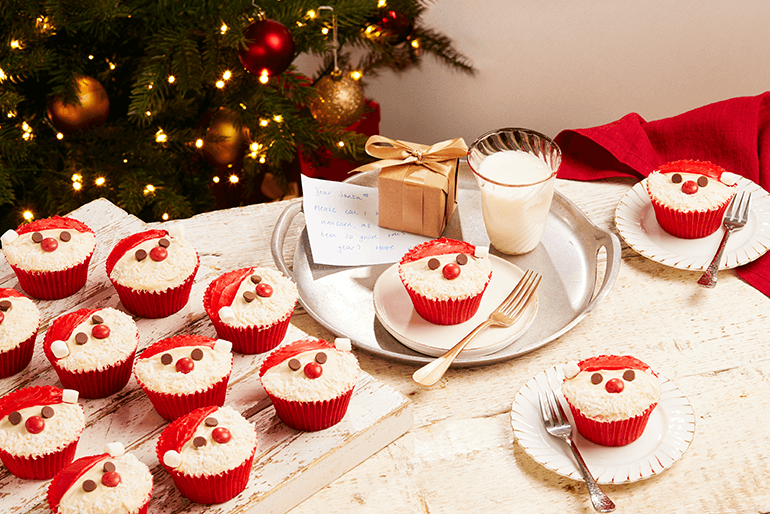 cupcakes for Santa topped with cream & chocolate chips displayed on plates on a Christmas themed table