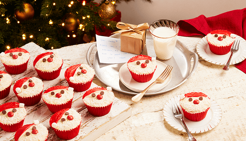 cupcakes for Santa topped with cream & chocolate chips displayed on plates on a Christmas themed table